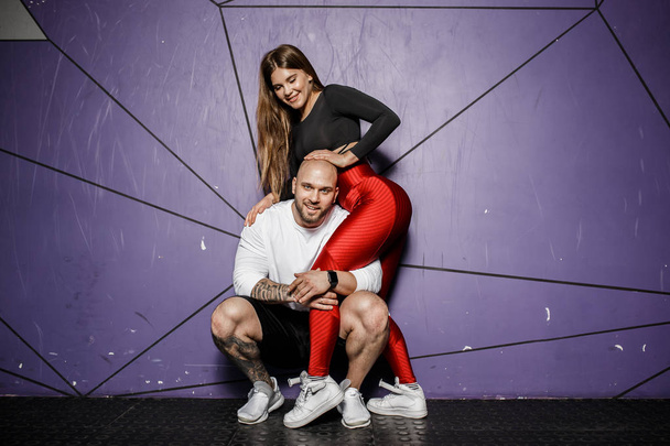 Cute athletic couple. Slender beautiful girl and strong athletic man in sports clothes are hugging on the background of stylish violet wall - Photo, Image