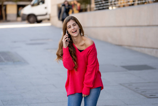 Pretty happy teenager woman talking on mobile smart phone outside city street. Beautiful stylish college student wearing fashion clothes feeling relaxed and free. Lifestyle, beauty and technology use. - Foto, Imagem
