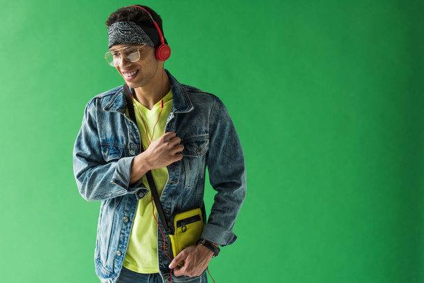 handsome mixed race man in headphones listening music and smiling on green screen with copy space - Fotoğraf, Görsel