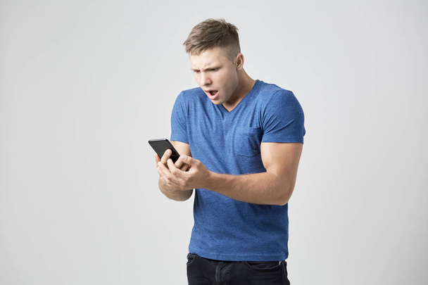 The guy dressed in blue t-shirt looks astonished at his mobile phone - 写真・画像