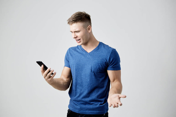 The guy dressed in blue t-shirt looks astonished at his mobile phone - Foto, imagen