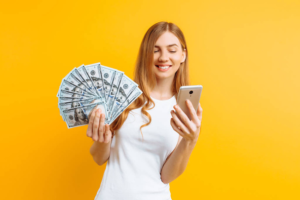 Portrait of an excited woman showing money bills and holding mob - Fotoğraf, Görsel