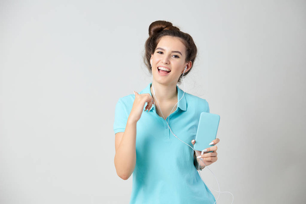 Joyful girl dressed in light blue t-shirt smiles and keeps mobile phone in her hand - Φωτογραφία, εικόνα