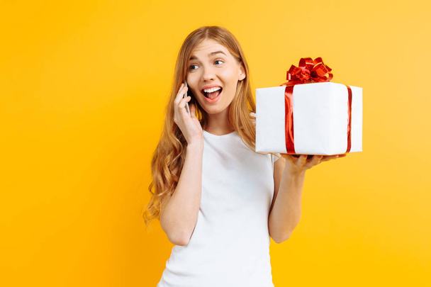 Happy young woman talking on a mobile phone, shows a gift box, o - Photo, Image