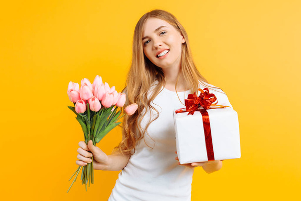 Happy girl holding a bouquet of beautiful flowers and a gift box - Foto, afbeelding