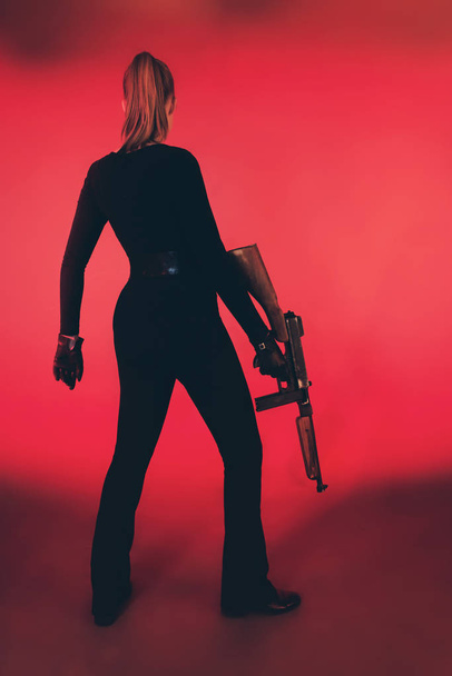 Mujer joven de pie con ametralladora sobre fondo rojo
. - Foto, imagen