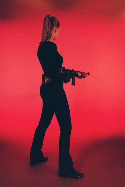 Young woman standing with machine gun against red background. - Photo, image
