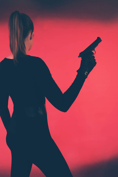 Woman with gun against red backround. - Valokuva, kuva