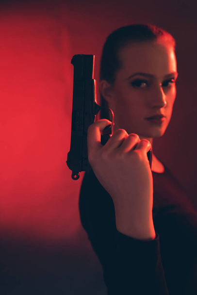 Blonde woman with pistol against red background. - Fotoğraf, Görsel