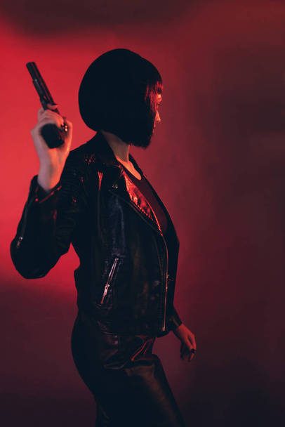 Woman with gun dressed in black against red background. - Photo, Image