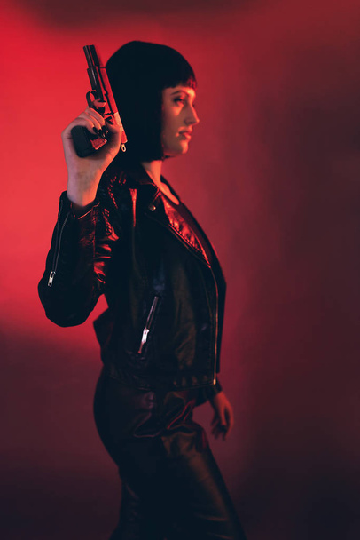 Жінка з пістолетом одягнена в чорне на червоному тлі
. - Фото, зображення