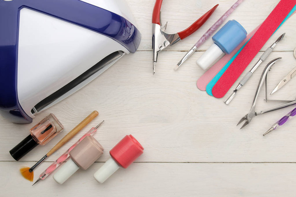 Maniküre. Nagellack, UV-Lampe und diverses Zubehör und Werkzeug für die Maniküre auf einem weißen Holztisch. Ansicht von oben - Foto, Bild