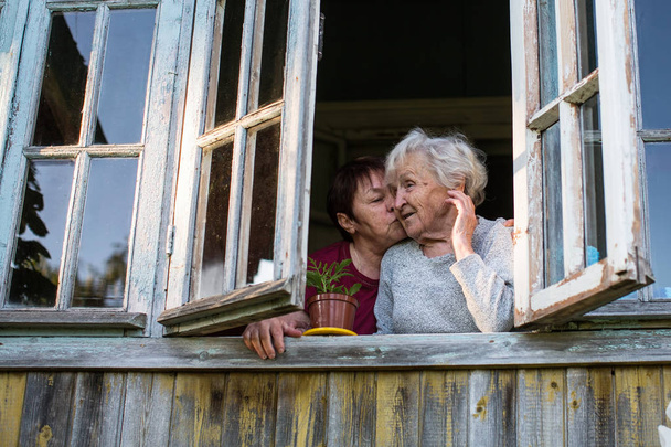 ältere Frau und ihre erwachsene Tochter aus dem Fenster des Dorfhauses. - Foto, Bild