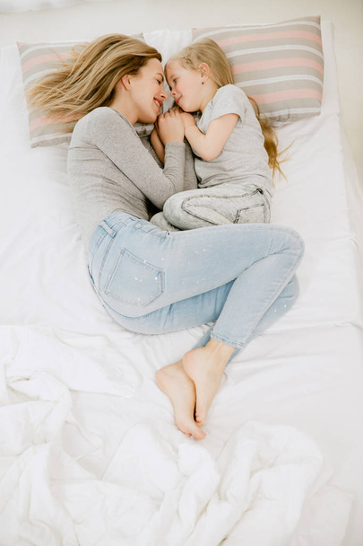 Nuori äiti ja hänen pieni tyttärensä halaavat ja suutelevat sängyssä
 - Valokuva, kuva