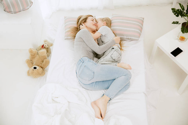 Young mother and her little daughter hugging and kissing on bed - Valokuva, kuva
