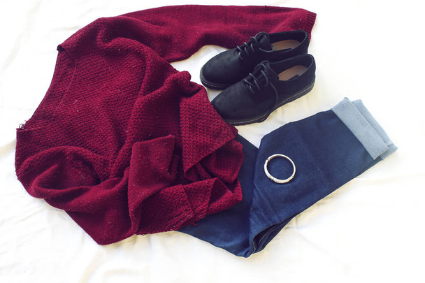 blue jeans, red oversize knitted sweater and black flat shoes, bracelet on white sheet. Overhead view of woman's casual day outfits. Trendy hipster look. - Photo, Image
