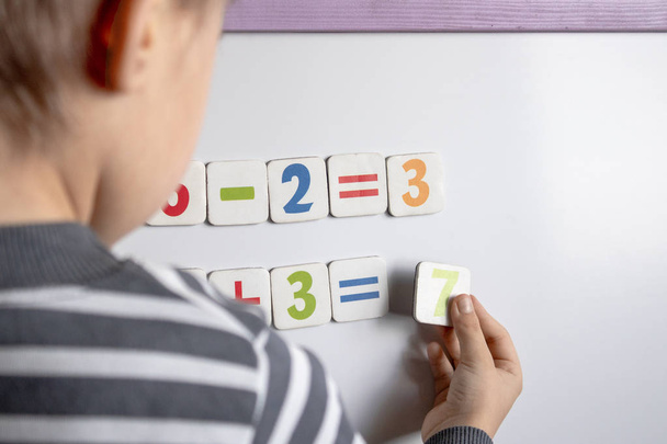 A little boy solves a difficult task. Against the background of the school board with numbers in their hands. - Photo, Image