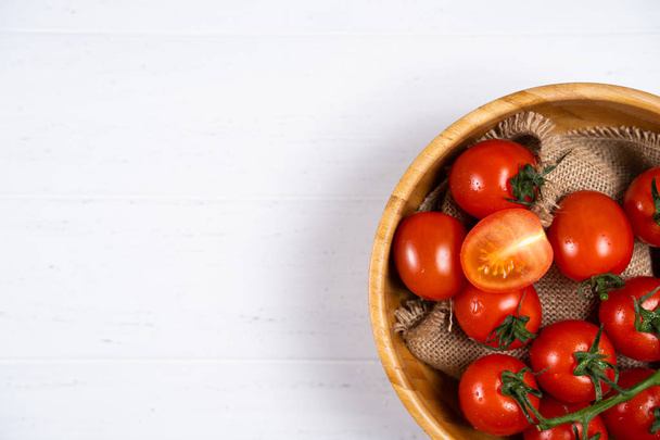 Tomates cerises fraîches dans une assiette en bois sur fond de bois blanc
. - Photo, image