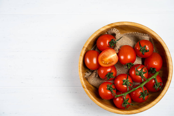 Beyaz ahşap zemin üzerinde ahşap bir tabak içinde taze kiraz domates. - Fotoğraf, Görsel