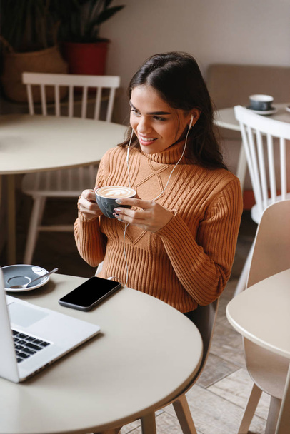 Bella donna seduta in un caffè al chiuso utilizzando il computer portatile
. - Foto, immagini