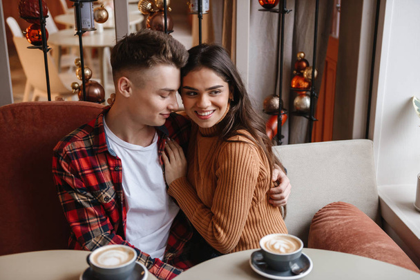 Cute young happy loving couple sitting in cafe indoors hugging. - Foto, imagen