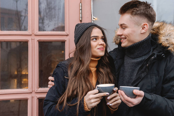 Young happy loving couple standing near cafe outdoors drinking coffee. - Foto, immagini