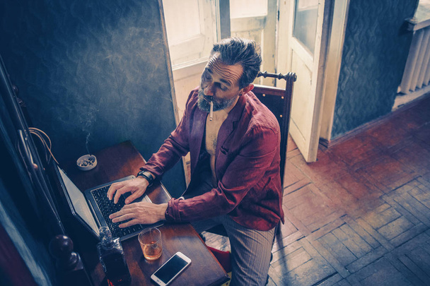 Handsome man works on his laptop smoking and drinking - Foto, Imagem