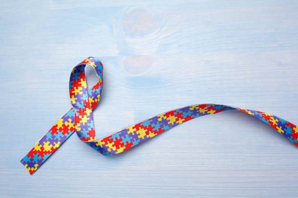 World Autism awareness and pride day with Puzzle pattern ribbon on blue wooden background - Photo, Image