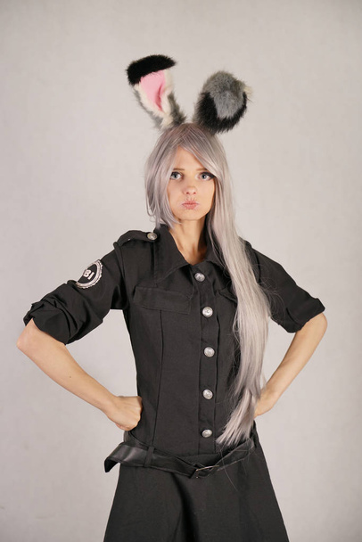 teen girl in FBI black carnival dress with big fur rabbit ears loves cosplay and stands on white Studio background - Photo, Image