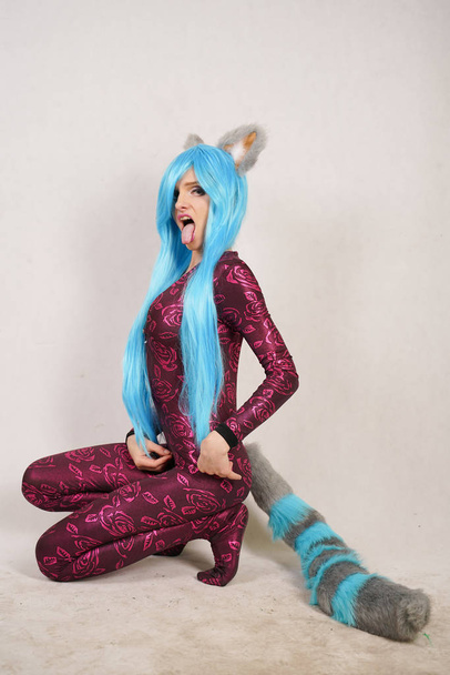 teen girl in an unusual jumpsuit with fur ears and a long fluffy tail loves cosplay and stands on a white Studio background - Photo, Image