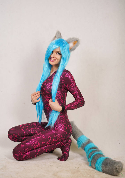 teen girl in an unusual jumpsuit with fur ears and a long fluffy tail loves cosplay and stands on a white Studio background - Photo, Image