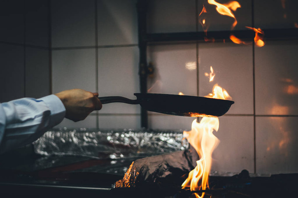 O chef cozinha e faz uma fogueira em uma panela. Cozinhar com fogo. C
 - Foto, Imagem
