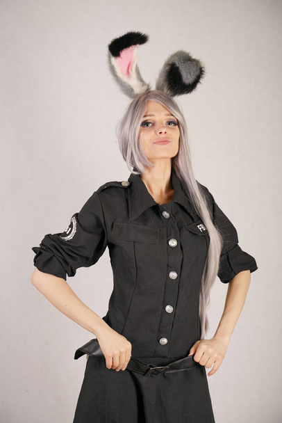 девушка-подросток в чёрном карнавальном платье ФБР с большими меховыми кроличьими ушами любит косплей и стоит на белом фоне студии
 - Фото, изображение