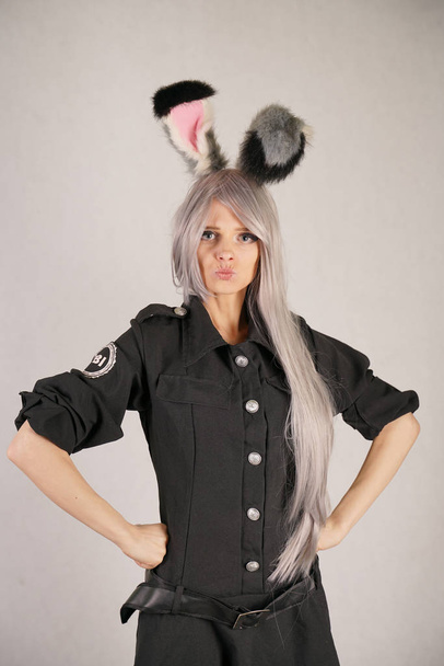 tiener meisje in Fbi zwarte carnaval jurk met grote bont konijn oren houdt van cosplay en staat op de witte achtergrond van de Studio - Foto, afbeelding