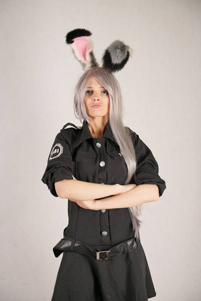 Teenie-Mädchen im fbi schwarzen Karnevalskleid mit großen Fellkaninchenohren liebt Cosplay und steht auf weißem Studiohintergrund - Foto, Bild
