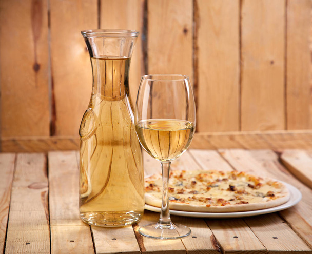 wineglass and decanter with cold white wine and pizza on wooden background, close-up   - 写真・画像