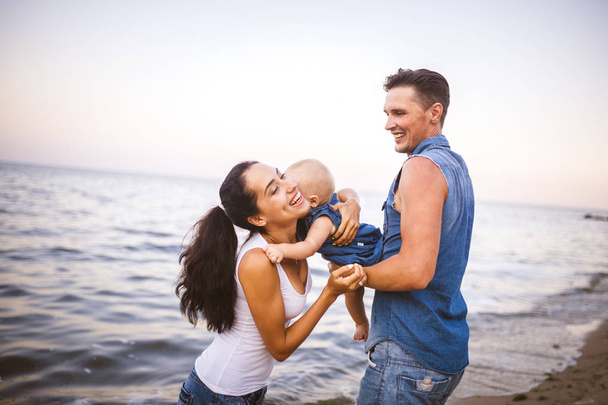 beautiful young family on vacation with baby. The father holds the blonde girl in her arms, and the brunette's mother hugs her husband. The concept of a family beach holiday summer near the sea - Photo, Image