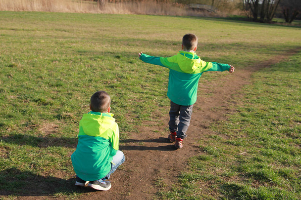 Boys, two, brothers in green windbreakers, go, view from the back - Φωτογραφία, εικόνα