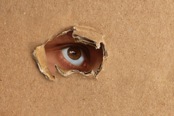 The human eye looks out of a hole in the cardboard, the concept of surveillance, peeping - Foto, afbeelding