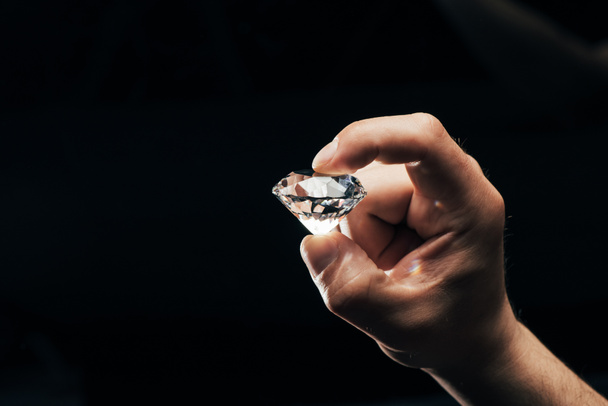 visão parcial do homem segurando grande diamante brilhante claro isolado em preto
  - Foto, Imagem