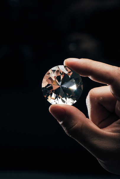 黒の背景に大きな透明な光沢のあるダイヤモンドを保持している男のトリミング ビュー - 写真・画像