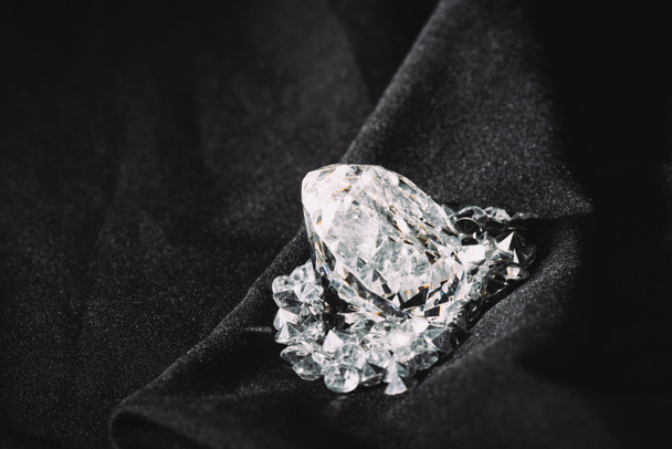 sparkling big diamond among small on black textured shiny cloth  - Φωτογραφία, εικόνα
