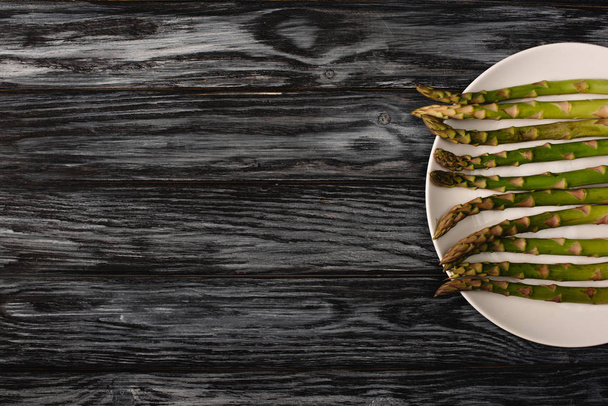 top view of green organic asparagus on plate on grey wooden background with copy space - Fotoğraf, Görsel