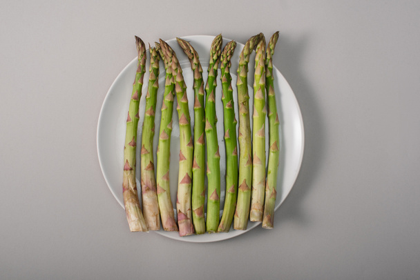 top view of green organic asparagus on plate on grey background - Foto, imagen