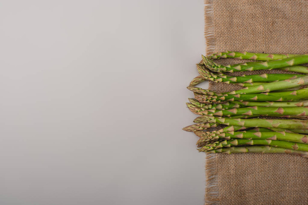 top view of green raw asparagus on sackcloth on grey background - Fotó, kép
