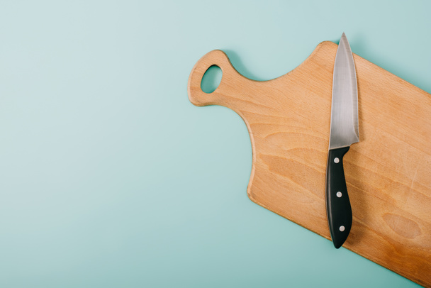 top view of wooden cutting board with knife on blue background  - 写真・画像