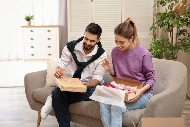 Young couple opening parcels on sofa in living room - Fotografie, Obrázek