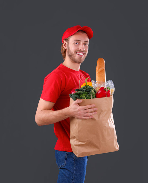 Delivery man holding paper bag with food products on dark background - Zdjęcie, obraz