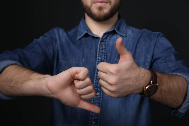 Człowiek pokazując kciuk w górę iw dół gest w języku migowego na czarnym tle, zbliżenie - Zdjęcie, obraz