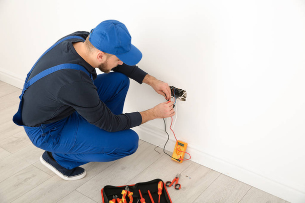 Electrician with tester checking voltage indoors, space for text - Foto, Imagen